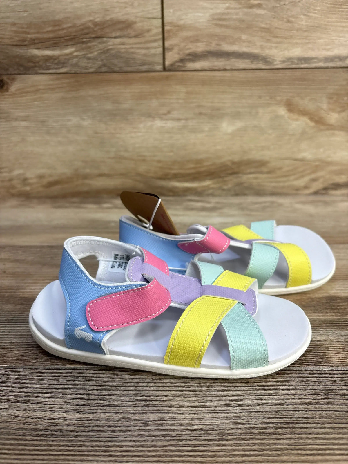 Side view of See Kai Run Shayna toddler sandals showing pastel pink, yellow, mint, and lavender straps with wood background