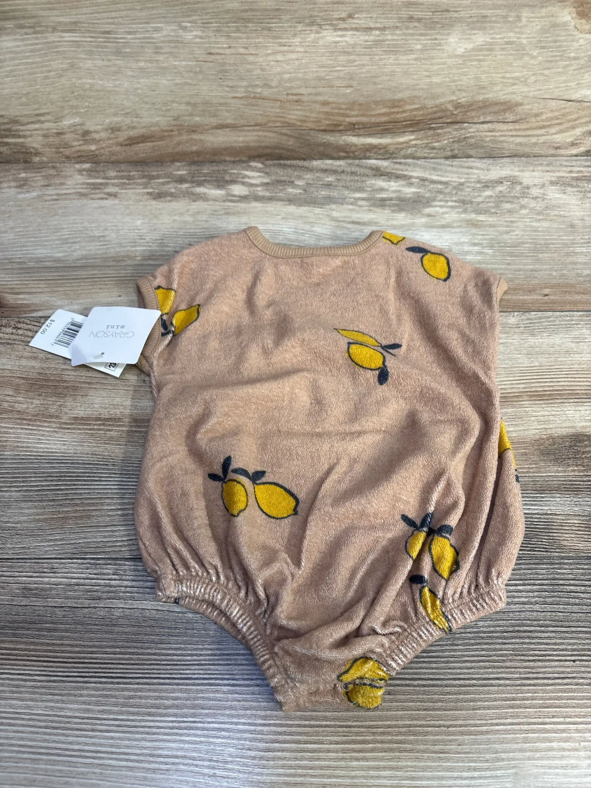 Top-down view of newborn brown terry cloth romper showcasing yellow lemon print and elastic leg openings on wood background