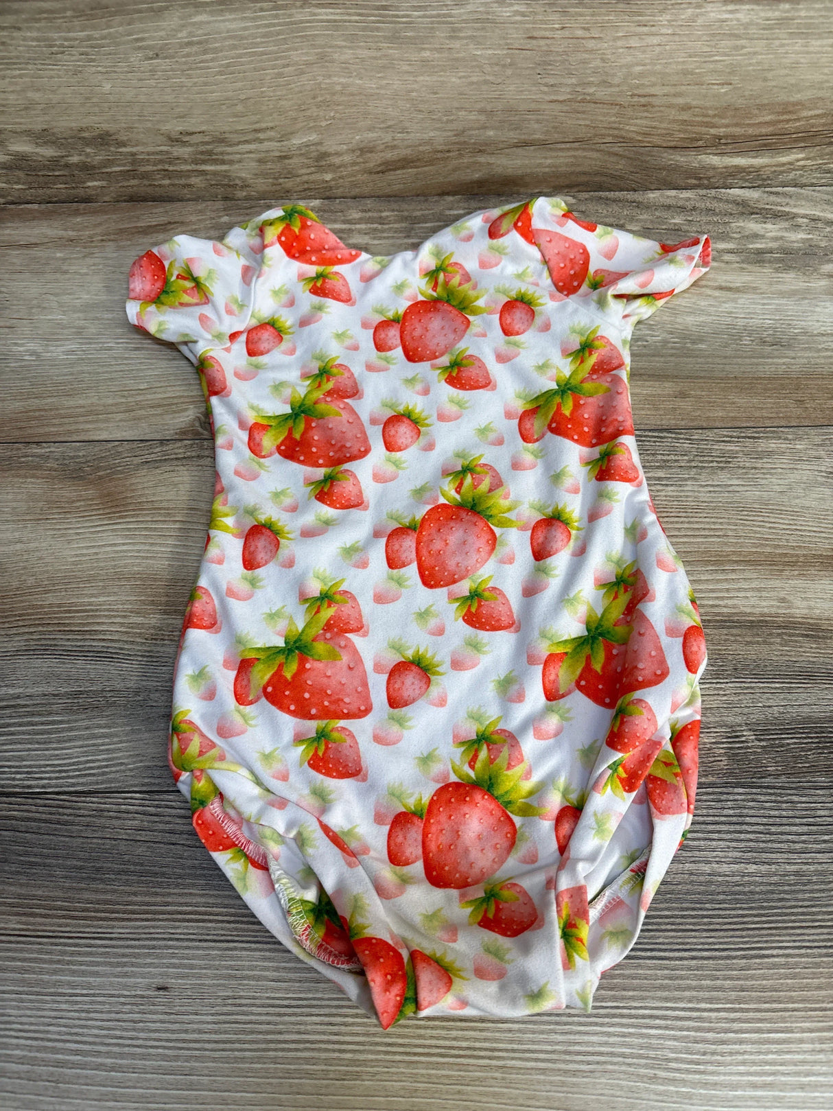 Strawberry print baby onesie with short sleeves on wood floor, cute kids clothing