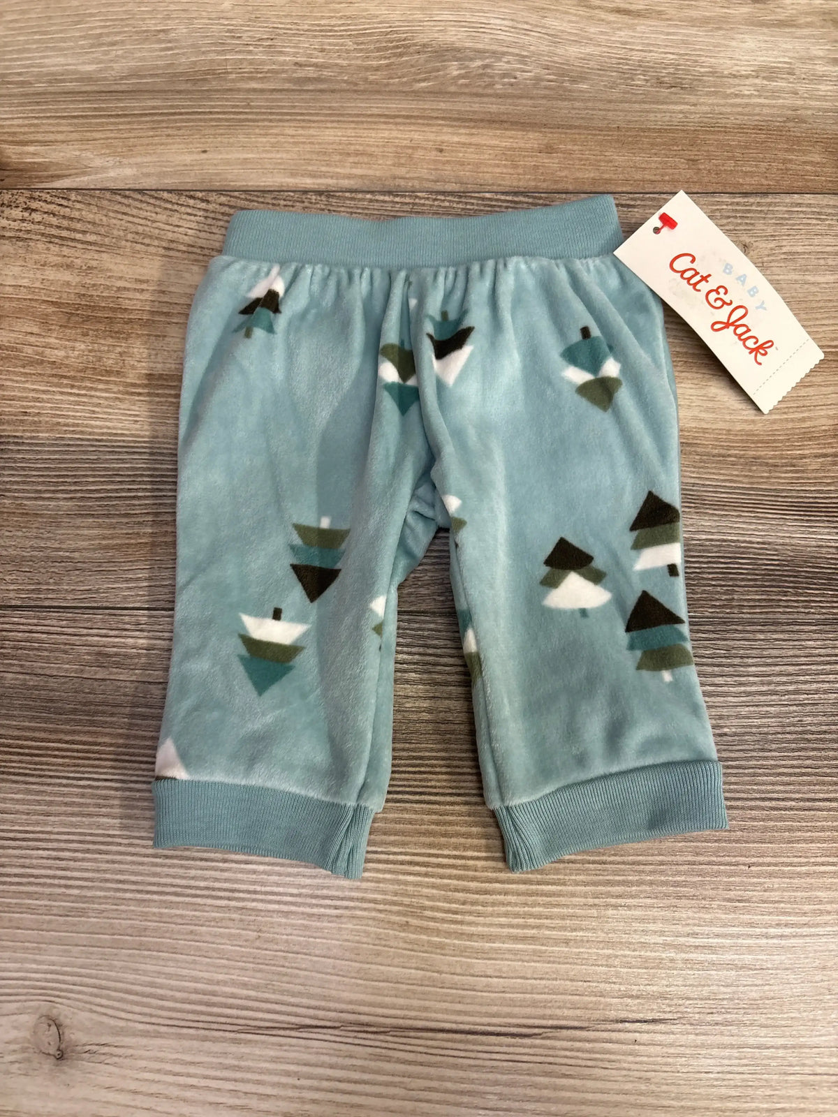 Blue fleece baby pants with tree print and Cat & Jack tag on wood background