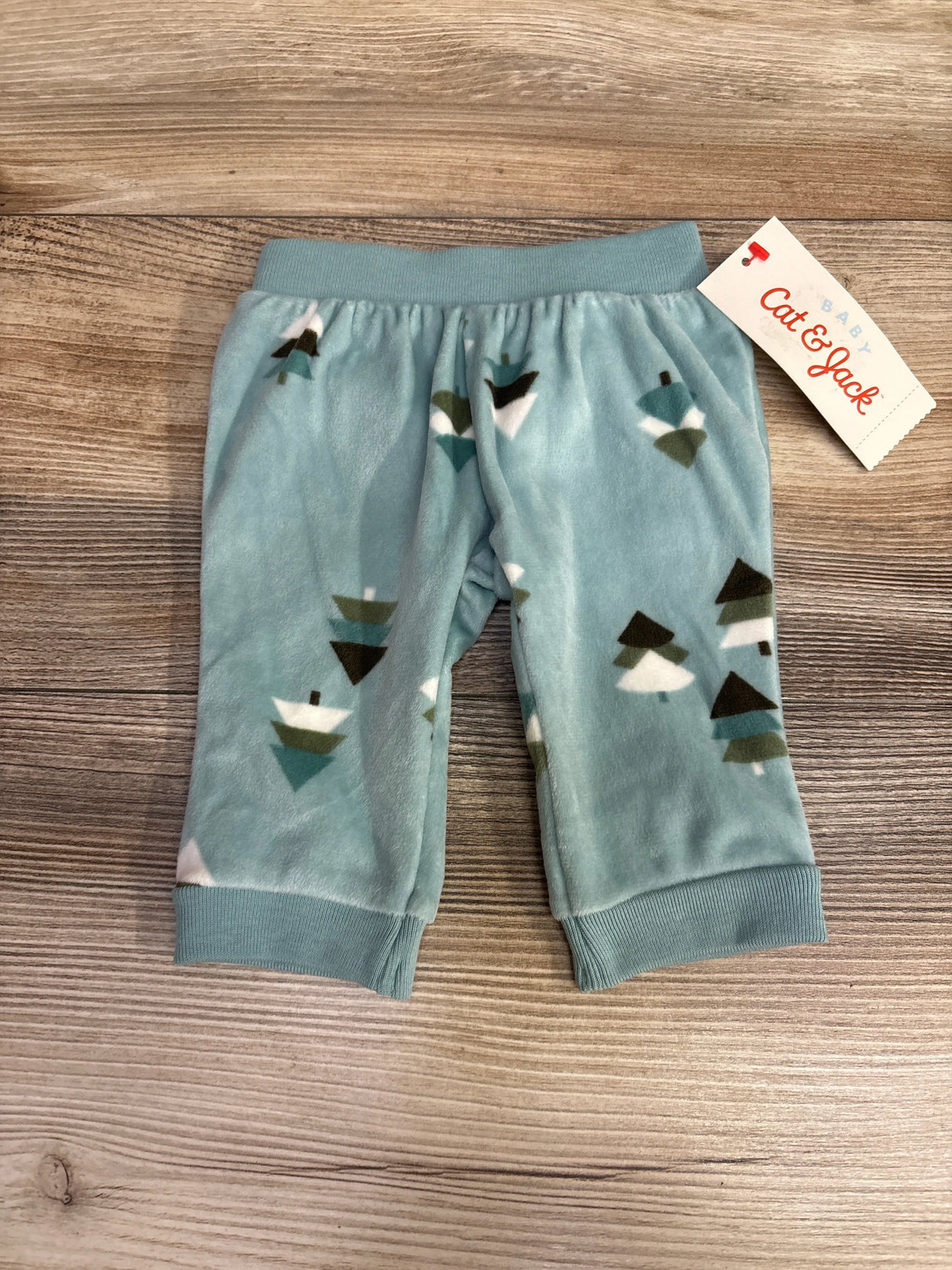 Blue fleece baby pants with tree print and Cat & Jack tag on wood background