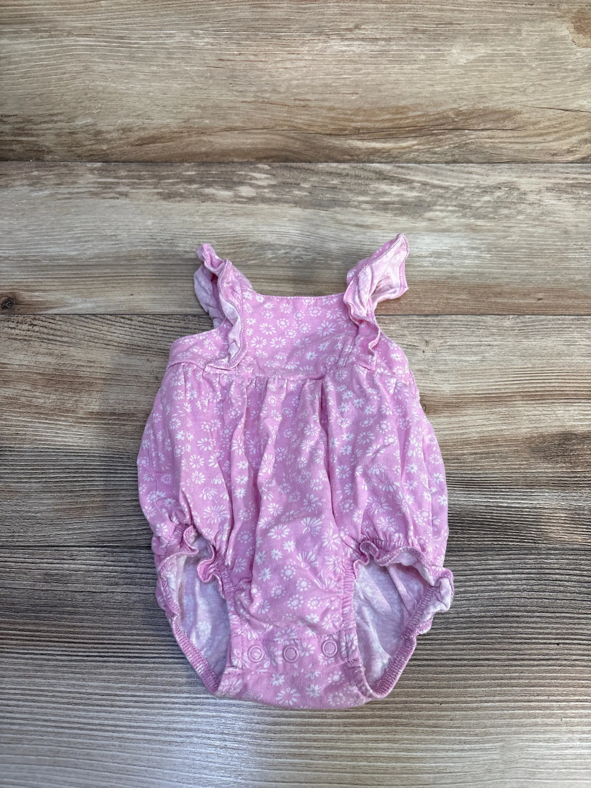 Front view of Carter’s pink floral bubble romper showcasing ruffled shoulder straps and snap closures with a wood-grain background