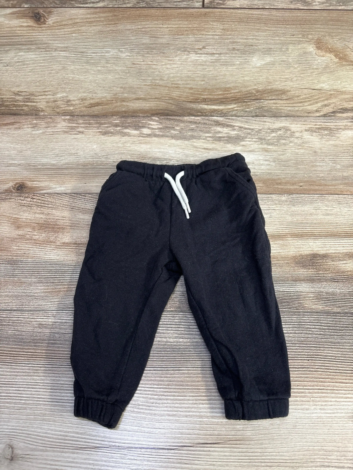 Front view of black Old Navy toddler joggers showing elastic waistband with white drawstring and cuffed ankles on wood floor