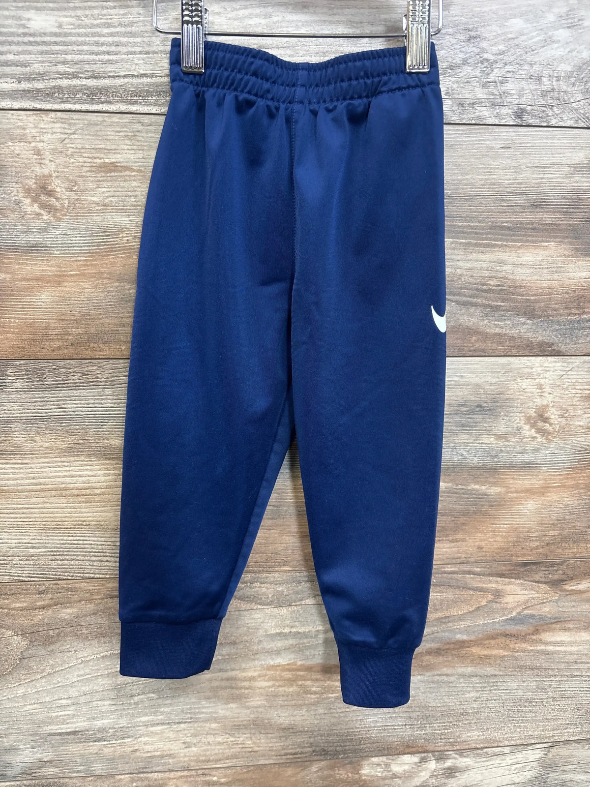 Navy blue toddler athletic pants with elastic waistband and white swoosh logo on wood background