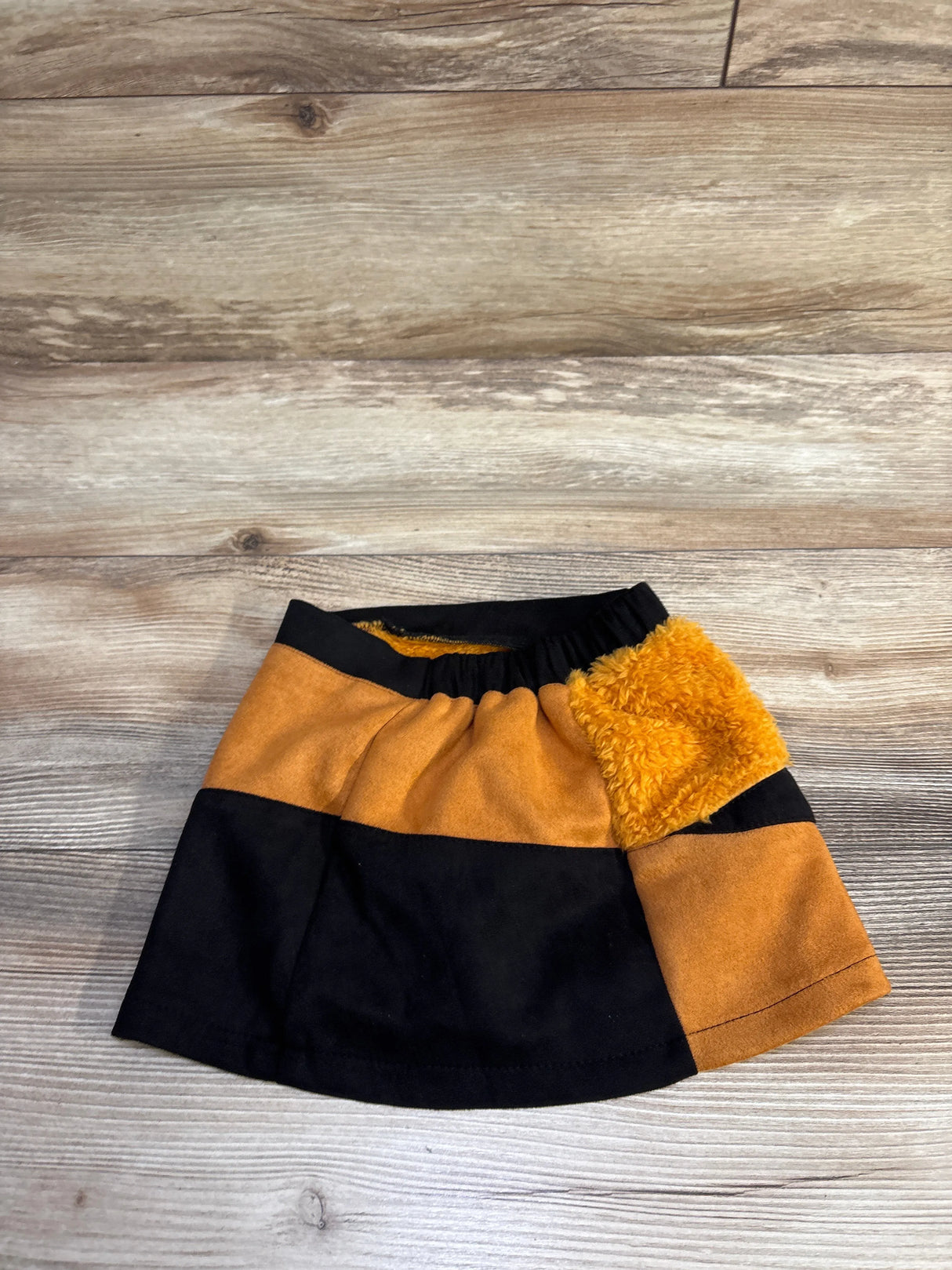 Flat lay of toddler colorblock faux-fur skirt in black-orange showing elastic waist and fuzzy side pocket on wood background