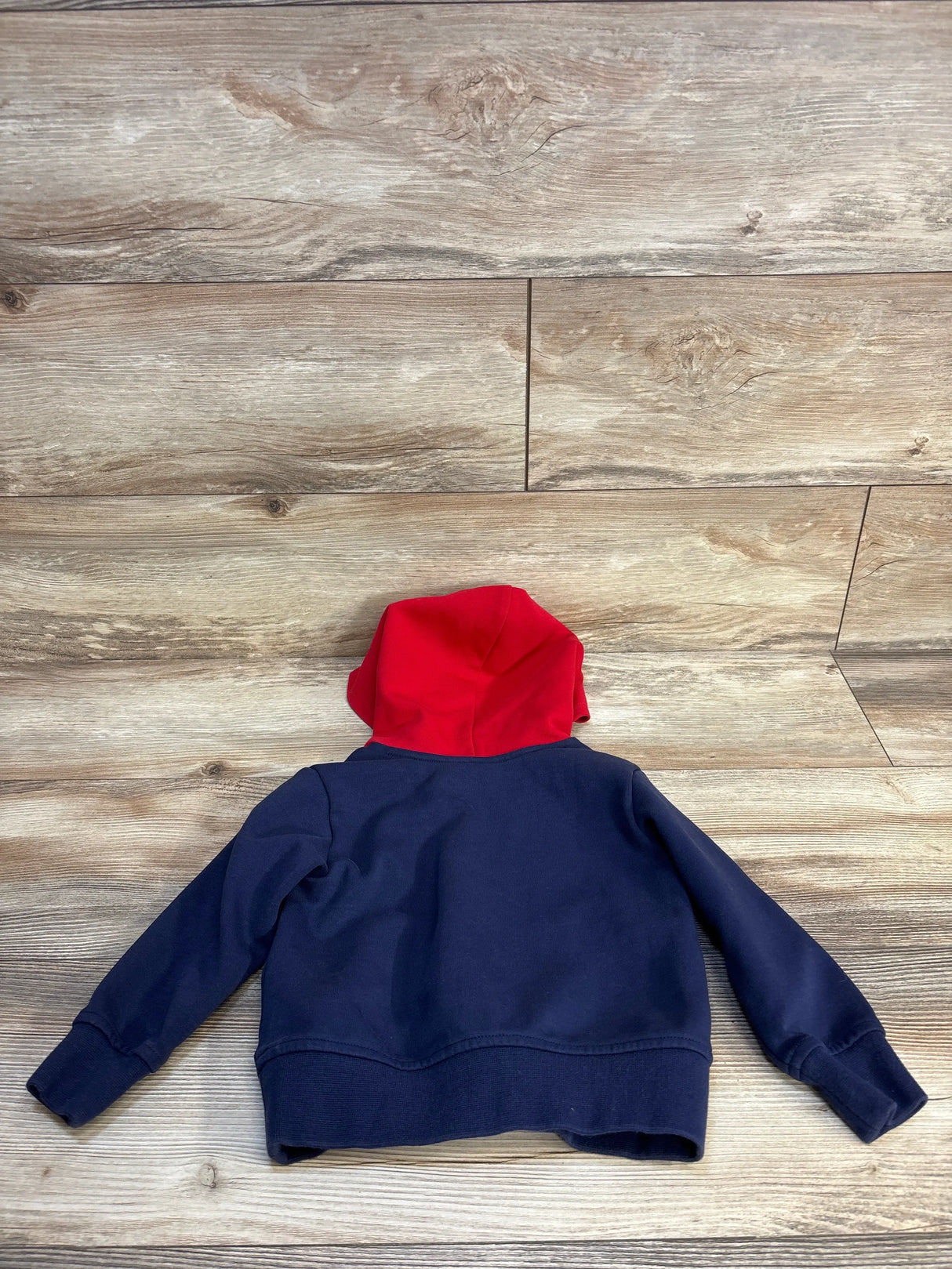 Navy blue kids hoodie with red hood, laid on wooden floor