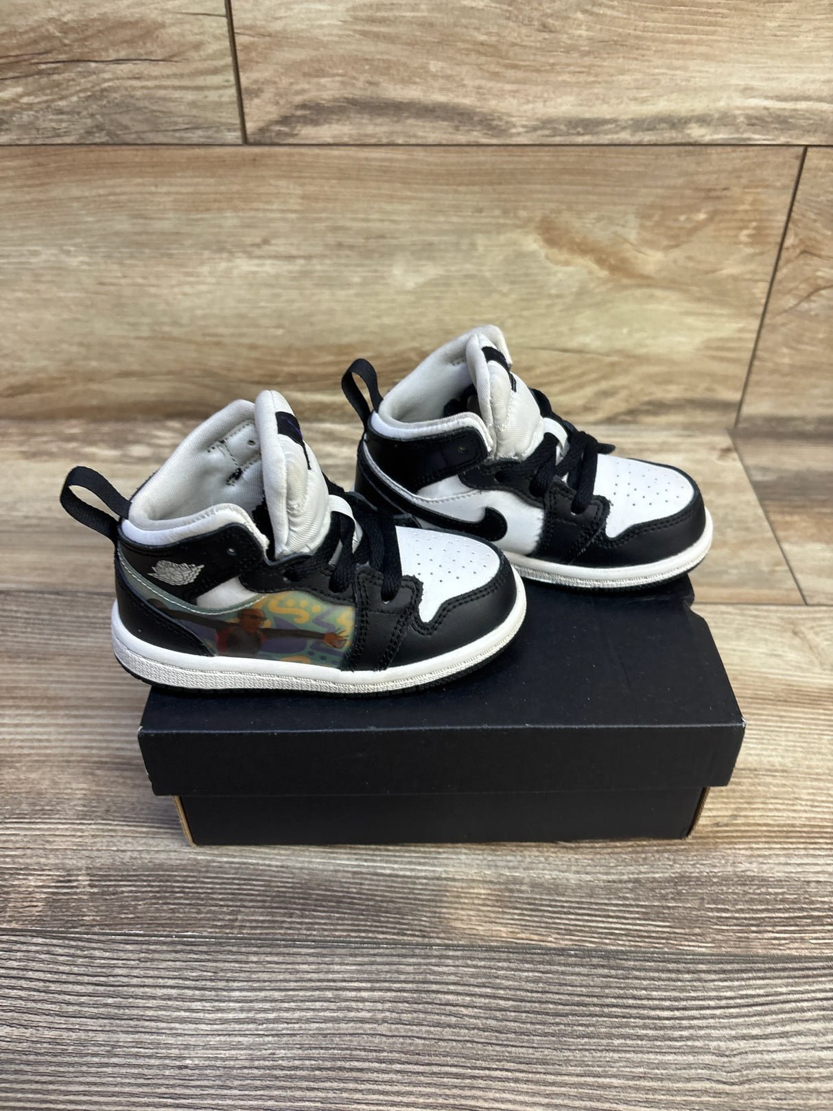 Side view of toddler Jordan 1 Mid Hologram sneakers in black and white showing holographic side panels on a black shoebox