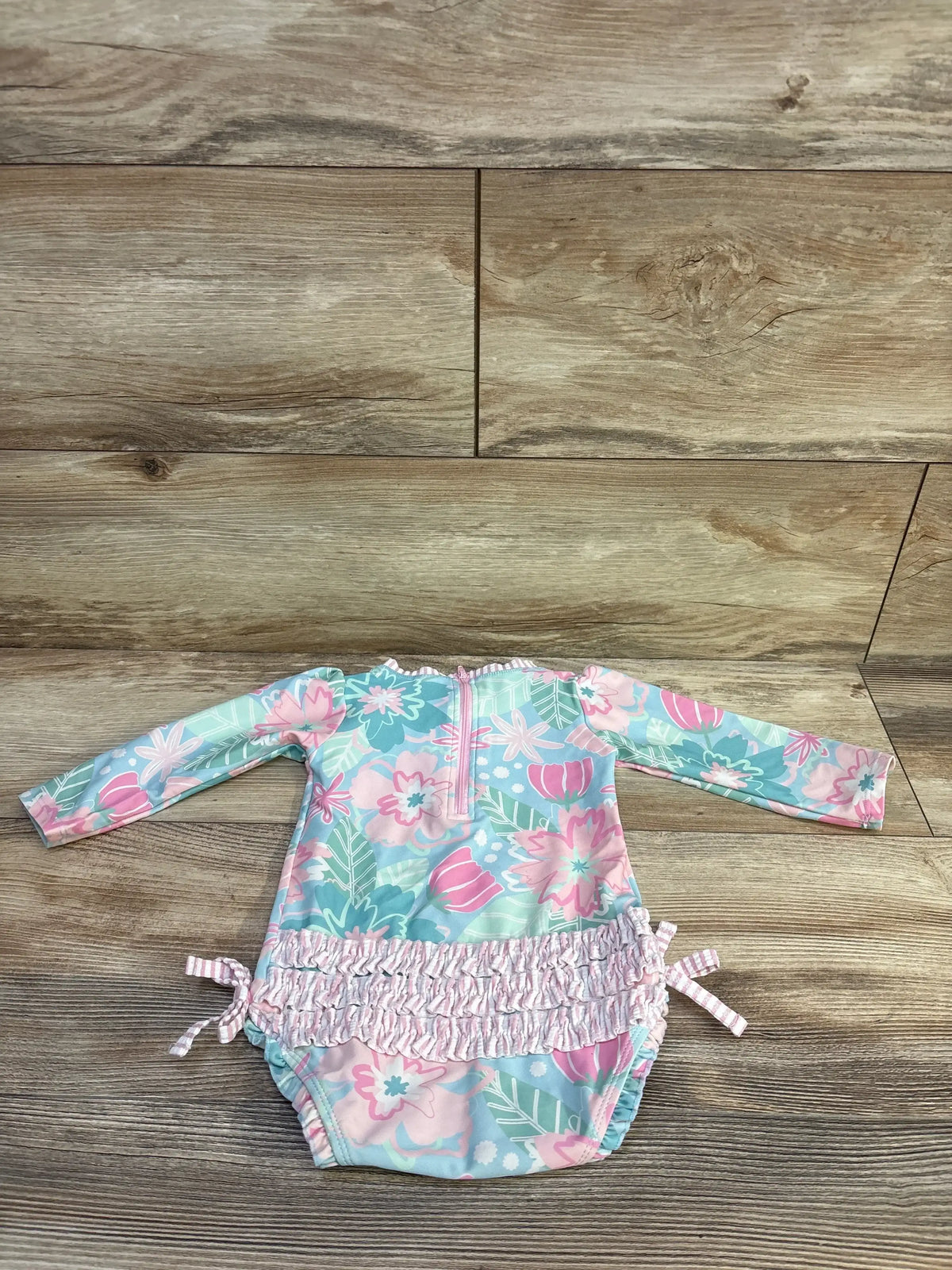 Flat lay of Ruffle Butts In Bloom one-piece rashguard swimsuit showcasing long sleeves, floral print, and ruffled waist