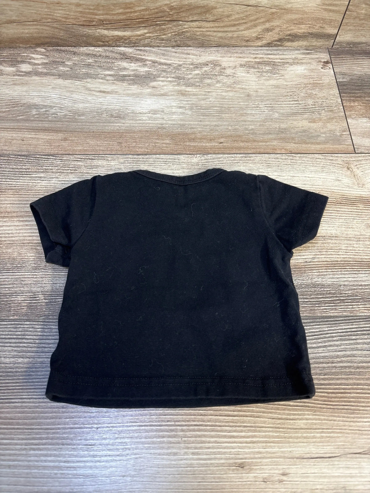 Black short sleeve baby t-shirt laid flat on wood background, rear view