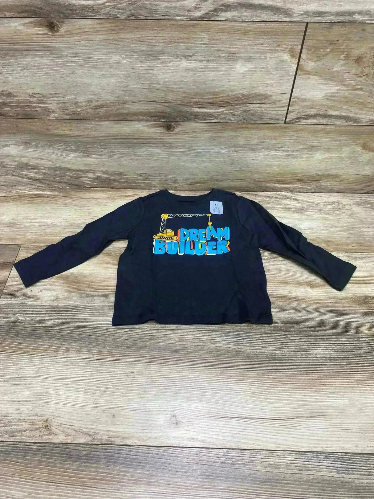 Front flat lay of Old Navy charcoal long-sleeve toddler shirt (2T) showing blue and yellow 'DREAM BUILDER' crane graphic on wood floor background