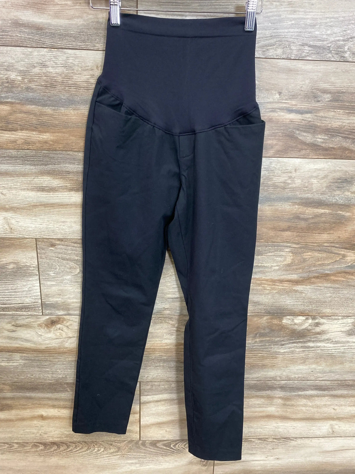 Front view of black Old Navy maternity Pixie ankle pants showcasing full over-the-belly panel and slim ankle fit on wood plank floor