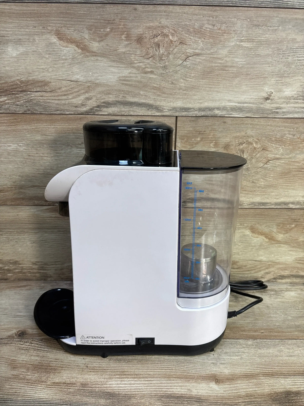 Front view of Baby EXO Smart Formula Maker/Dispenser with transparent measured reservoir and black lid against wood backdrop