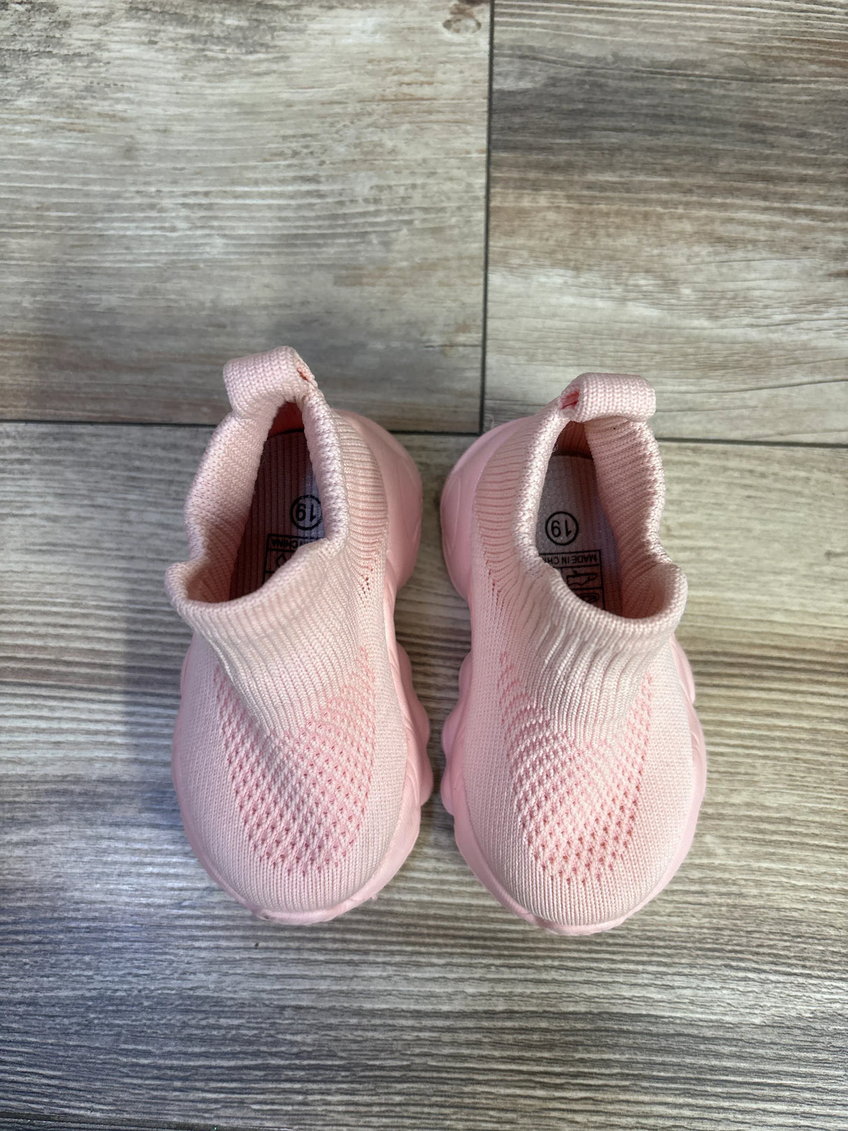 Top-down view of pink high-top mesh sock baby shoes showing knit texture, pull tabs, and cushioned soles on wood floor