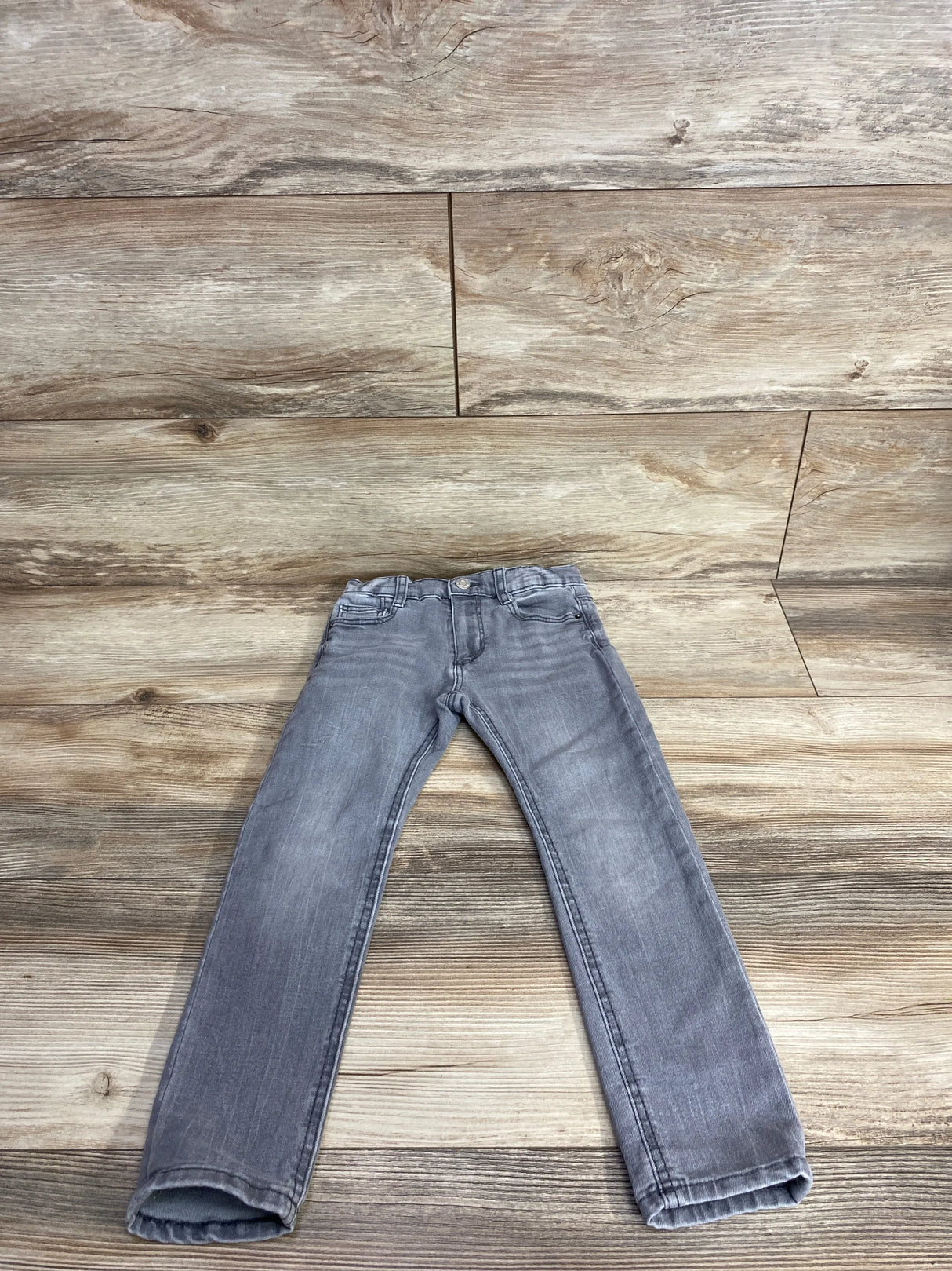 Gray kids jeans with pockets laid flat on wooden floor background
