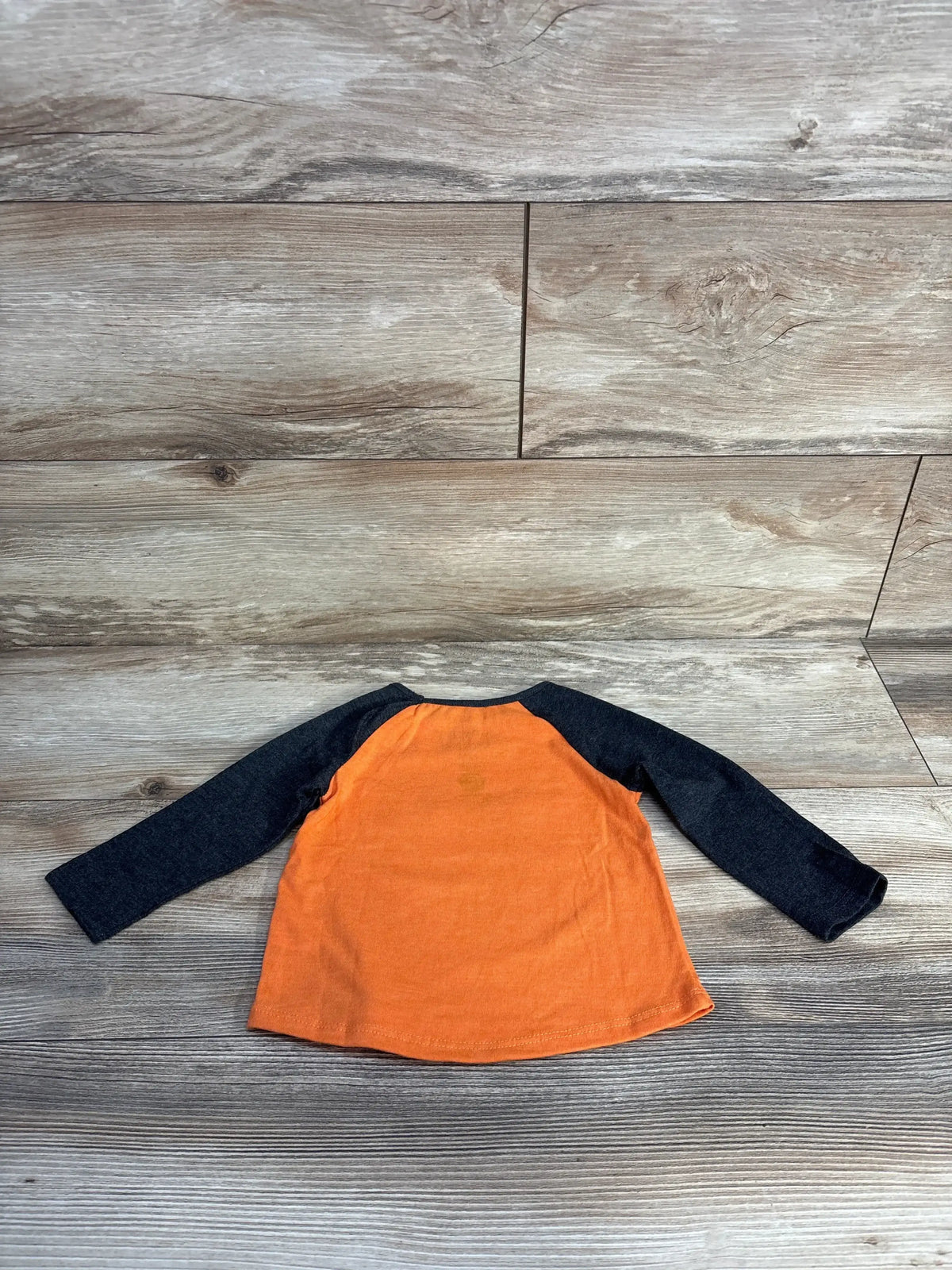 Back view of Jumping Beans Paw Patrol raglan shirt in grey and orange, showcasing dark raglan sleeves on wood-look flooring