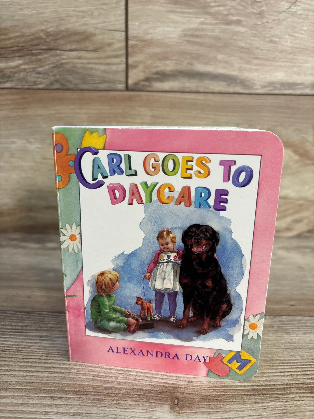 Front cover of Carl Goes to Daycare Board Book showing Carl the rottweiler with children on a colorful cover on a wooden floor