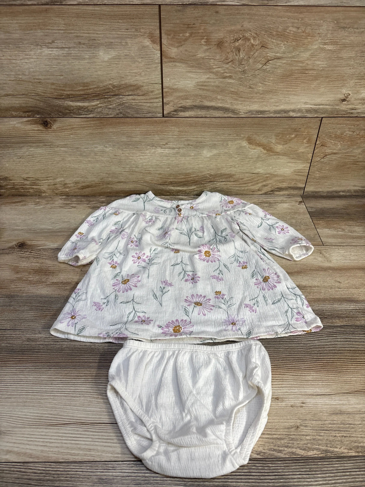 Flat-lay of Carter's white Henley dress with matching bloomers showing pink daisy print and elastic waist on wood background