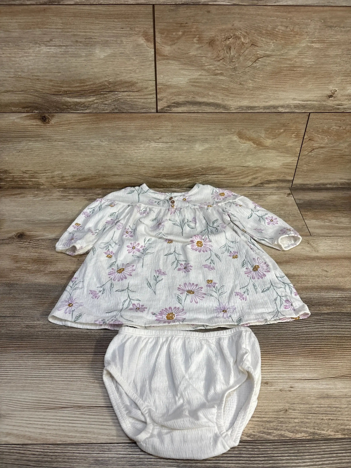 Flat-lay of Carter's white Henley dress with matching bloomers showing pink daisy print and elastic waist on wood background
