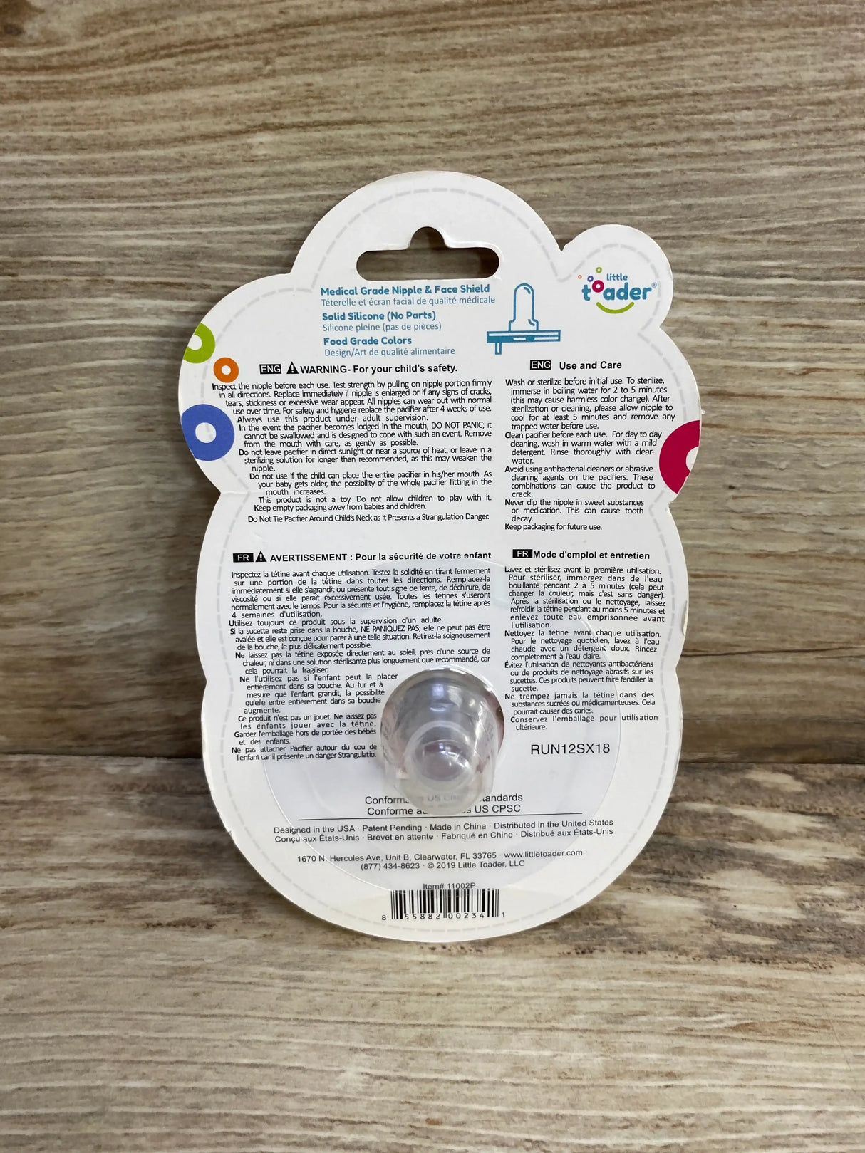 Back of Little Toader Cupcake pacifier (pink, 3m+) in clear blister pack showing printed instructions on wood background