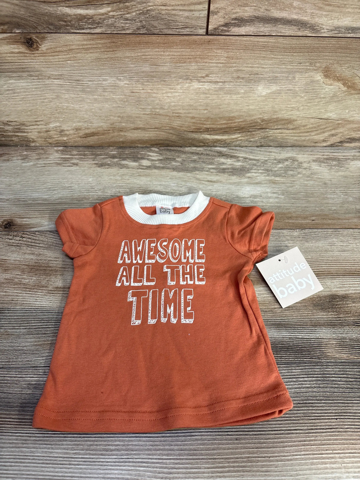 Front view of orange Attitude Baby shirt with white collar, ruffled sleeves, and Awesome All the Time text on wood