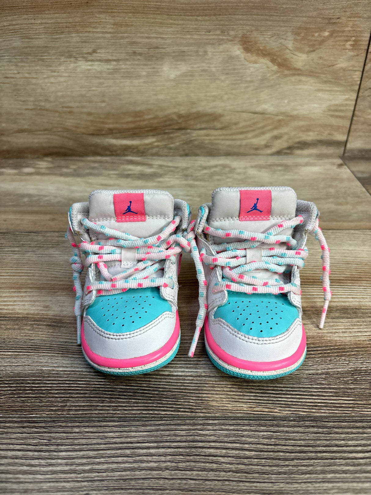 Baby blue, white, and pink Nike Air Jordan sneakers on a wooden floor