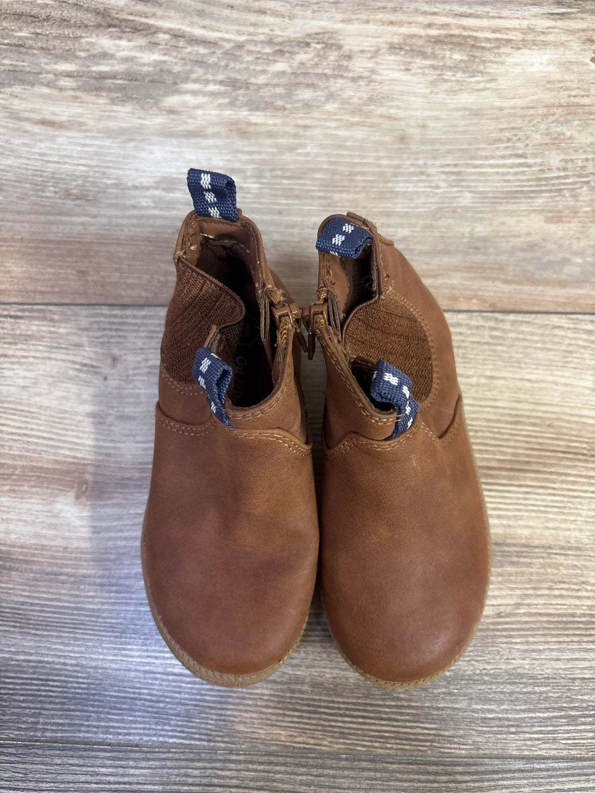 Top view of Cat & Jack toddler brown zipper boots showing side zippers, elastic ankle panels and navy pull tabs on wood floor