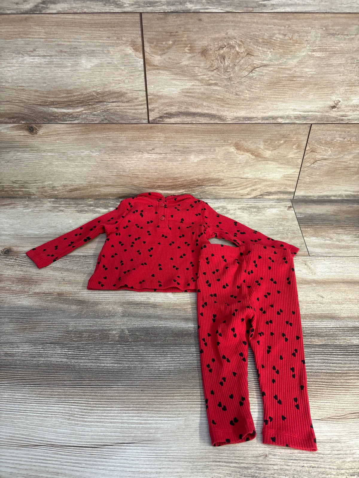 Front view of Baby Gap rib heart shirt and pants set in red showcasing ribbed knit and allover black heart print on wood-look floor