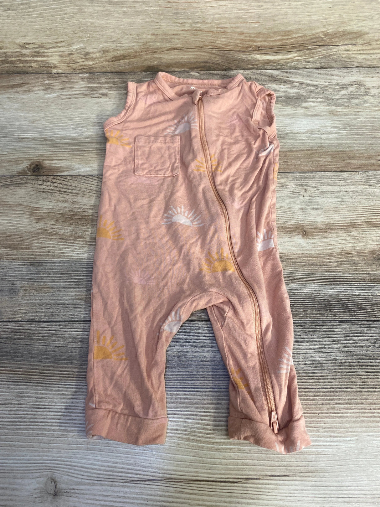 Flat lay of peach Kyte Baby sleeveless bamboo zip romper (6-12m) showing front zipper, chest pocket, and sun print on wood background