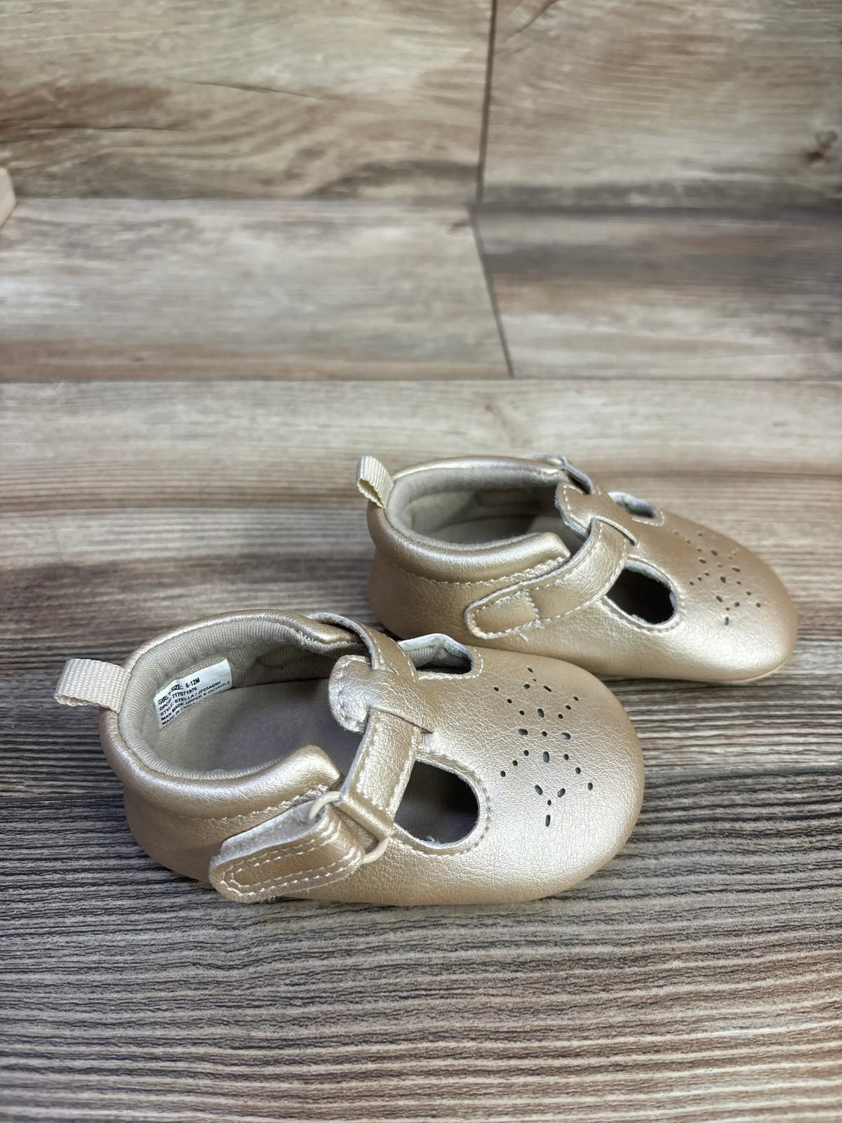 Three-quarter view of gold Just One You Stella pre walker sandals with closed toes and hook-and-loop straps on wood grain