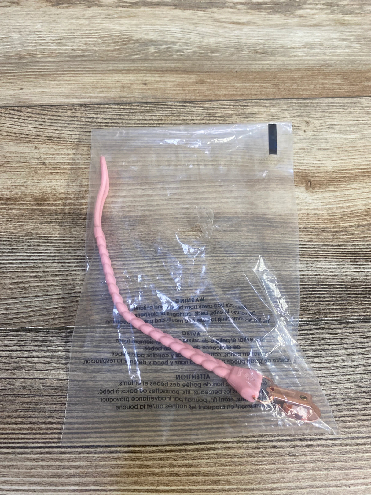 Pink plastic spiral tail accessory in clear packaging on wood background