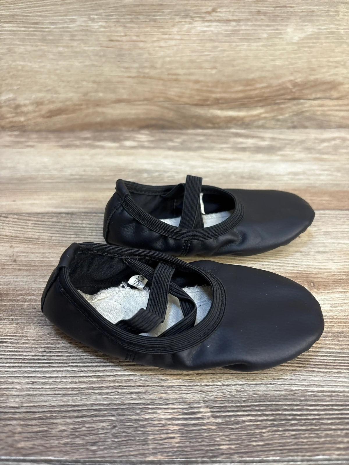 Black toddler ballet flats with elastic straps on wood background, gently used kids shoes