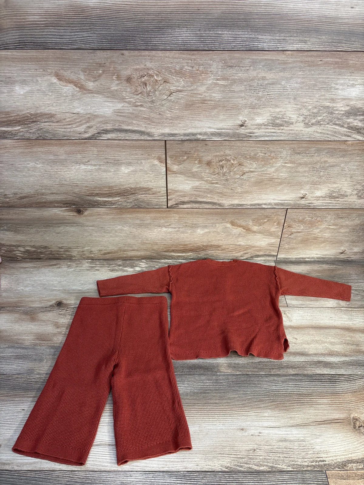 Flat lay of Modern Moments rust waffle knit henley shirt and pants set showcasing textured fabric on a wood floor