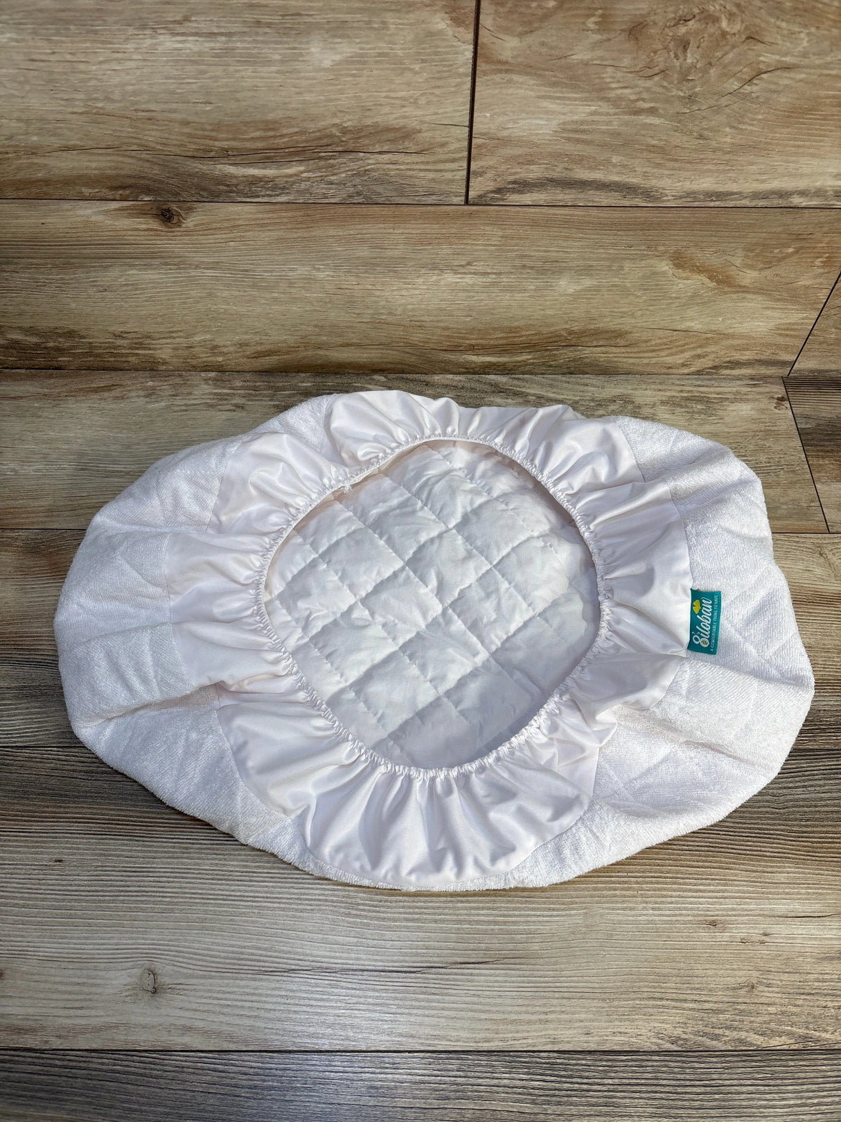 White quilted bassinet pad cover with elastic edges on wood floor, baby bedding accessory