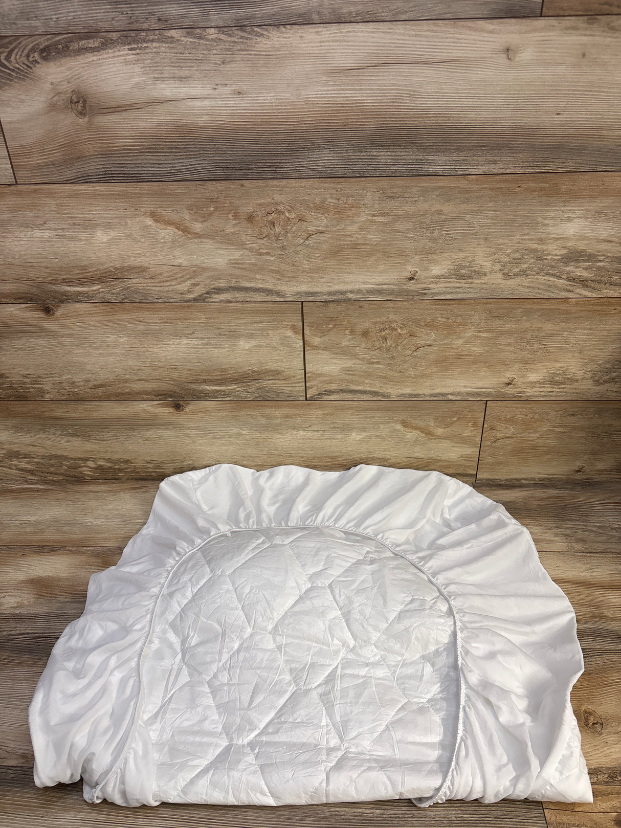 Top view of Amfori crib mattress protector showing quilted waterproof center and elastic fitted skirt on wood floor