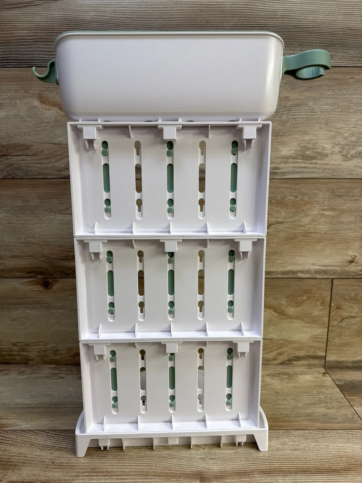 Front view of Momcozy DIY Large Baby Bottle Drying Rack showing three open drying tiers with green hooks on a wood floor
