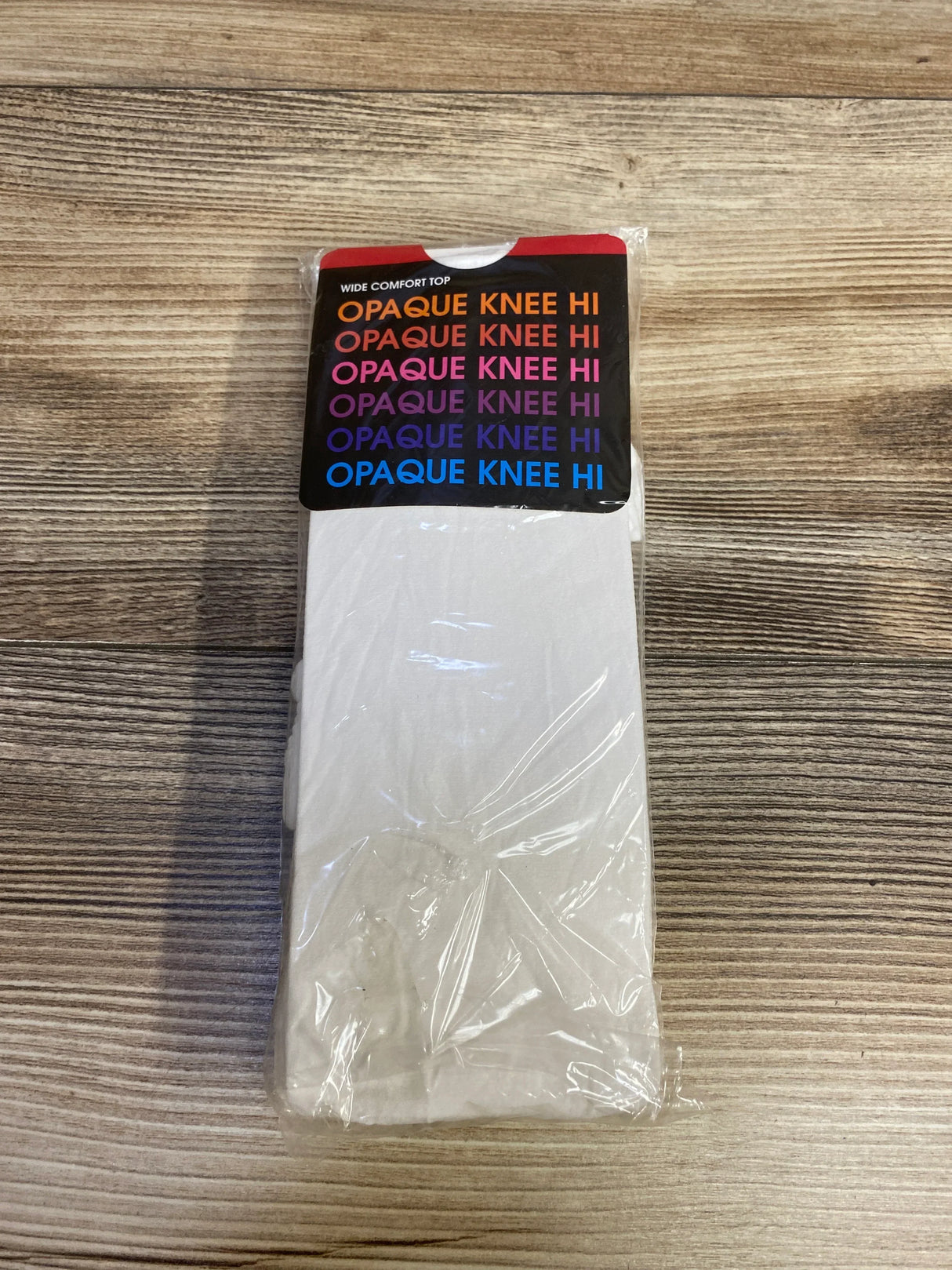 White opaque knee high socks in plastic packaging on wood surface, wide comfort top label