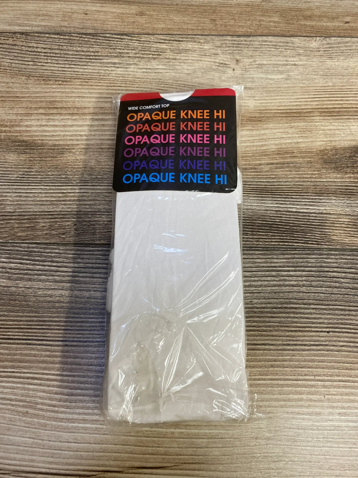 White opaque knee high socks in plastic packaging on wood surface, wide comfort top label