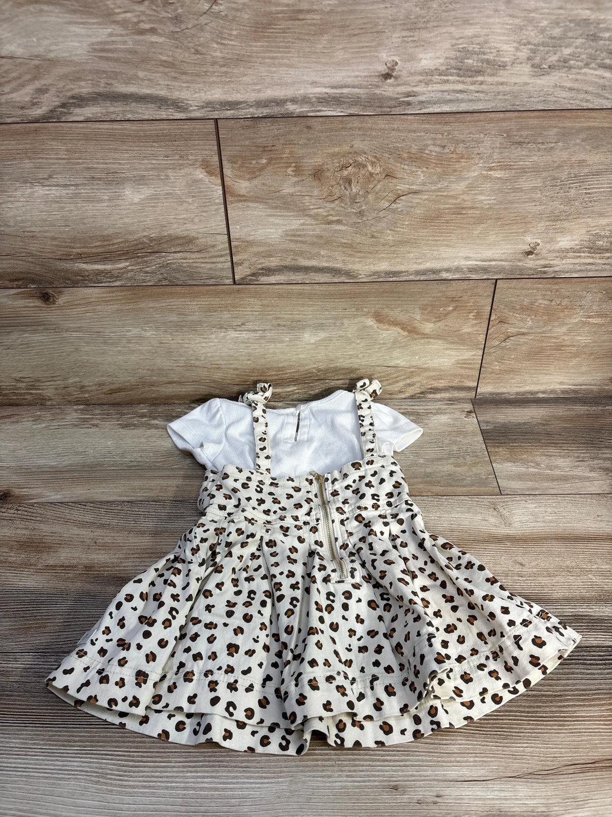 Top view of 7 For All Mankind two piece toddler set showcasing white ribbed shirt and leopard skirtall on a wood floor