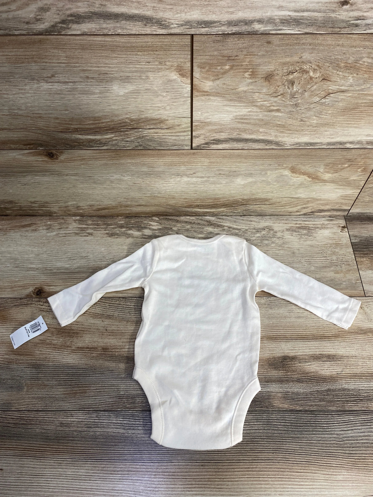 White long-sleeve baby onesie on wooden floor, soft and cozy for newborns