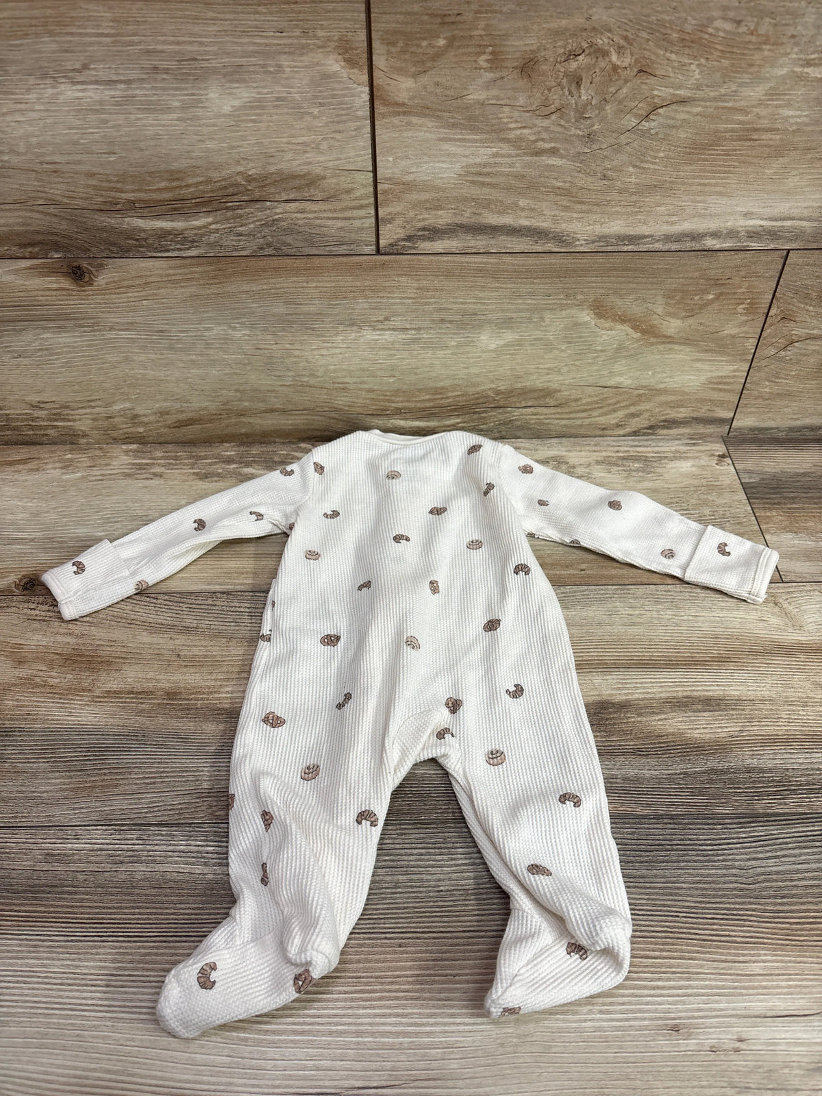 Top-down view of Carter’s ivory waffle knit sleeper showcasing footed legs and brown print on wood flooring