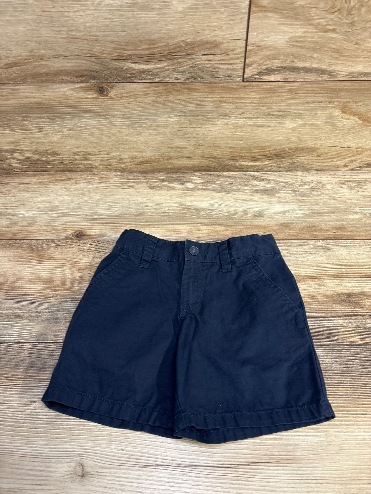 Front flat lay of children’s navy Cat & Jack school uniform shorts showing button-front waist, belt loops and side pockets on light wood floor