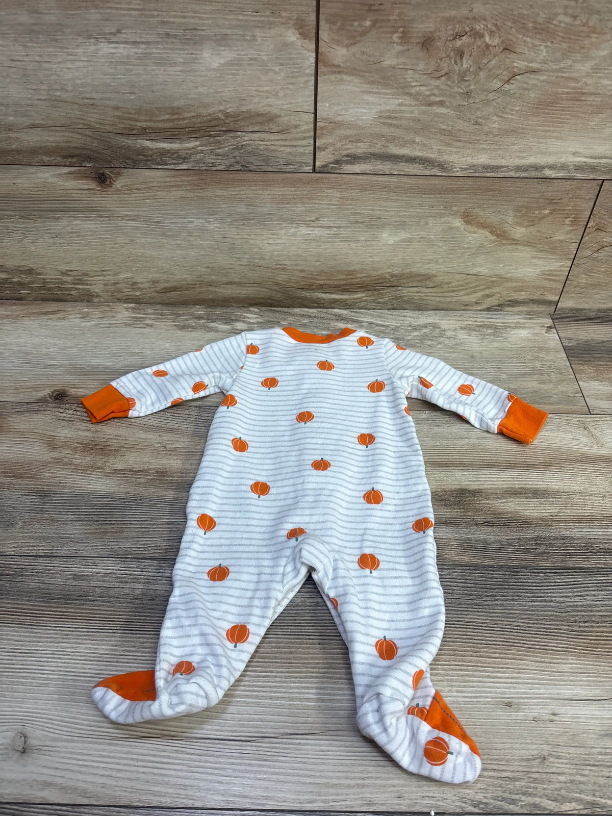 Flat lay of white Simple Joys Pumpkin Snap Sleeper with gray stripes, orange pumpkins, and orange cuffs on wood flooring
