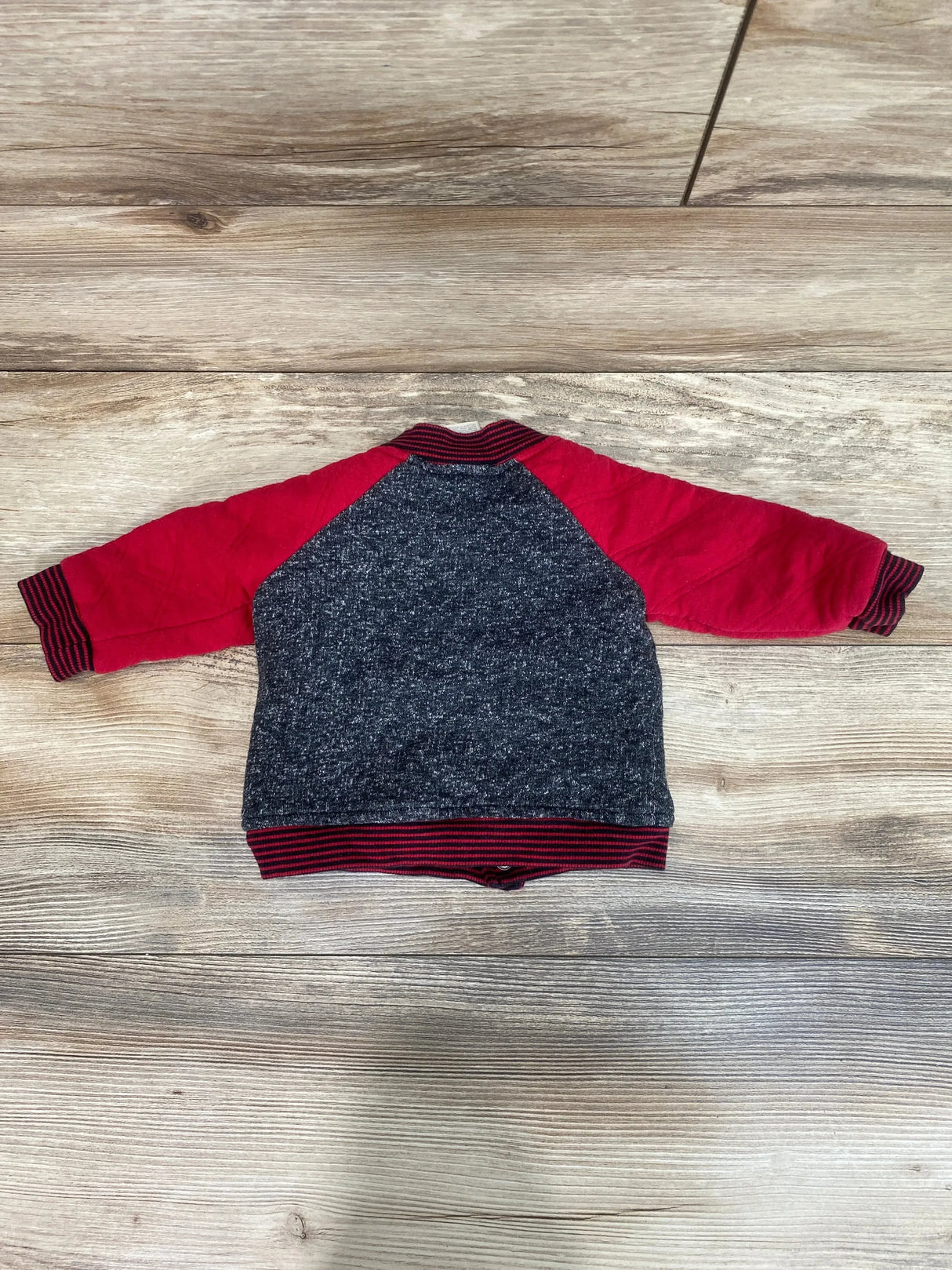 Back of First Impressions jacket, size 3-6m, red raglan sleeves, heathered gray body and ribbed cuffs on wood floor