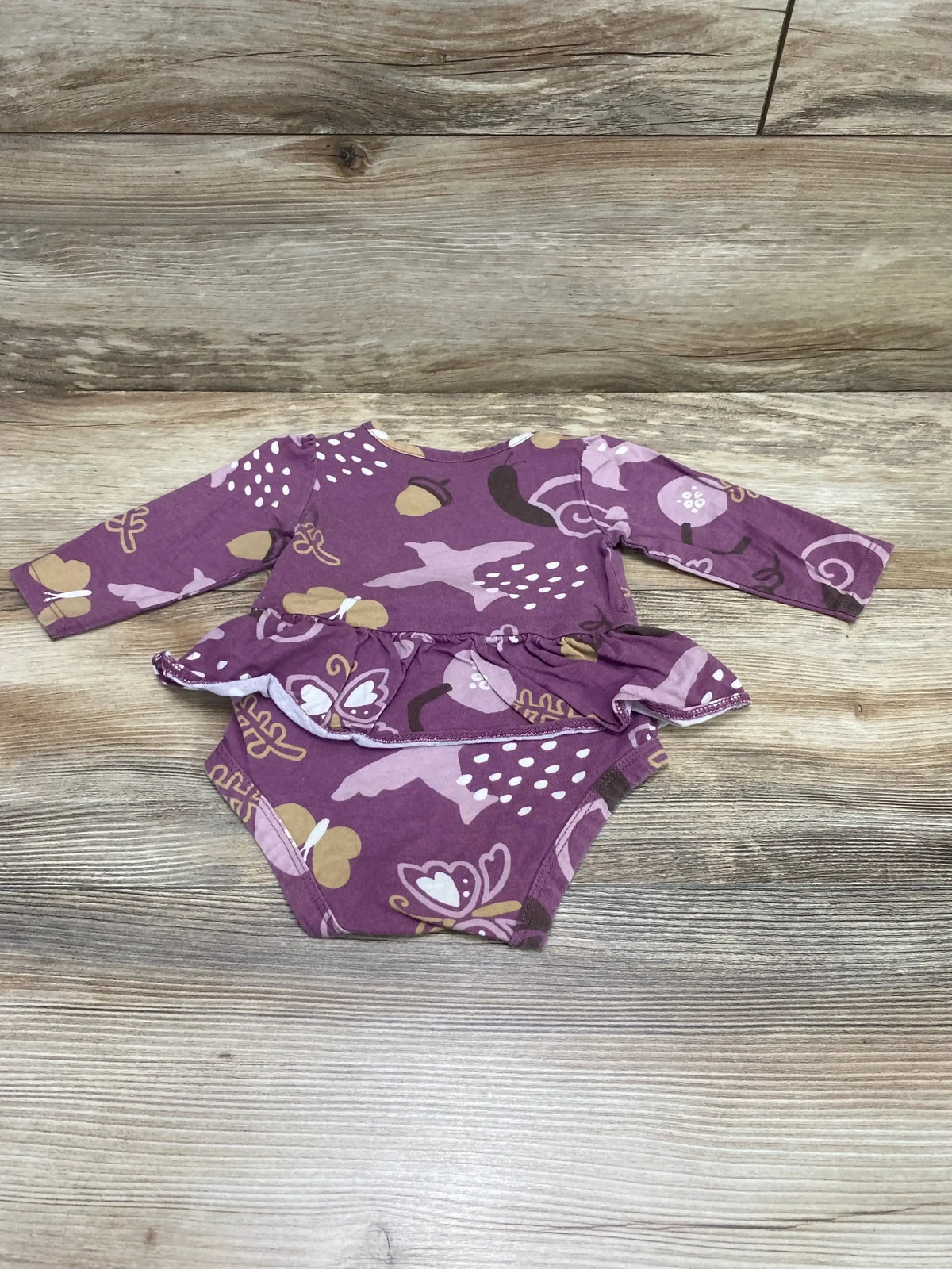 Flat lay of Carter’s purple long-sleeve skirted bodysuit size 6M showing ruffle skirt and butterfly print on wood background