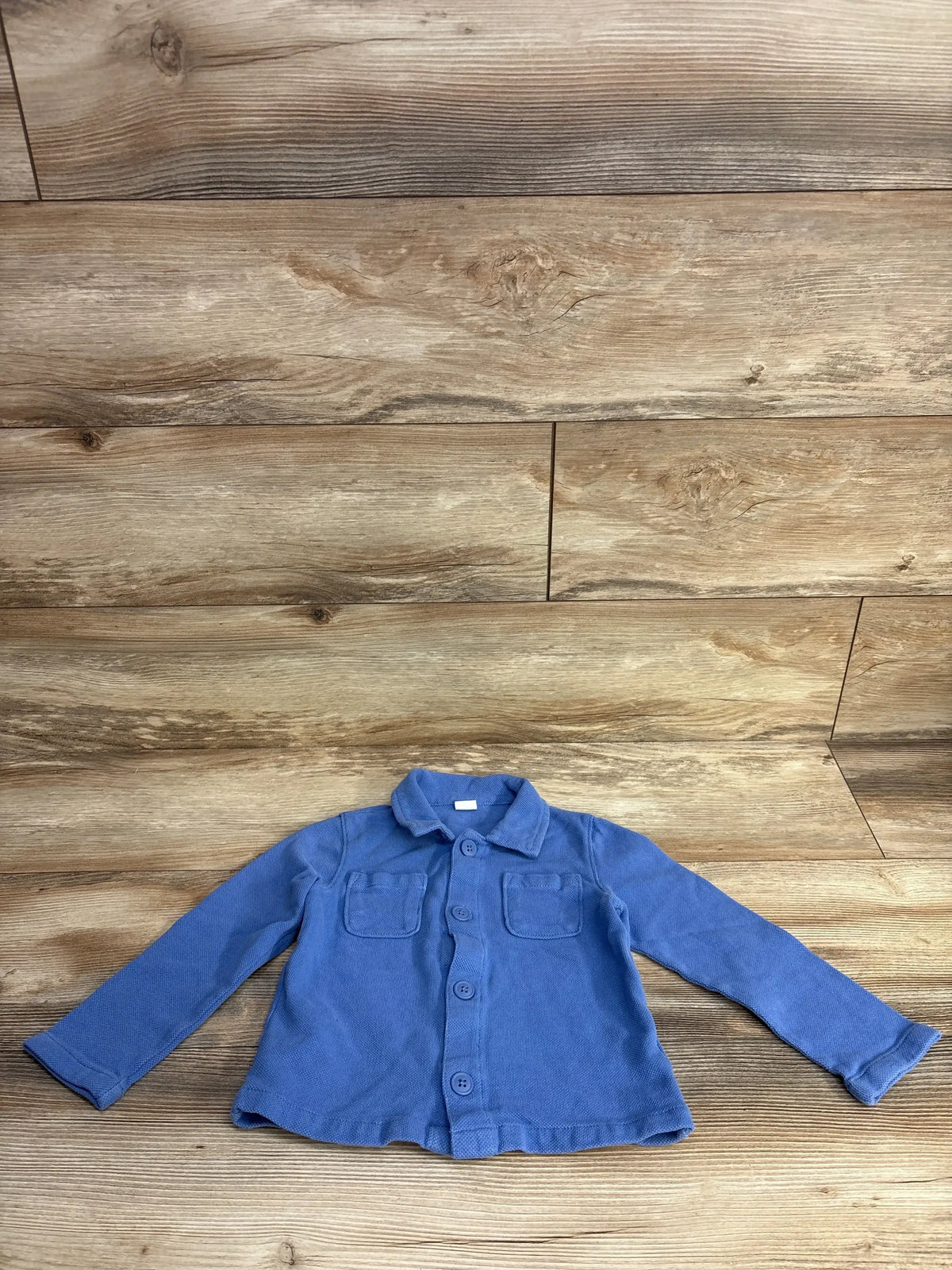 Blue long sleeve toddler shirt with buttons and chest pockets on wood background