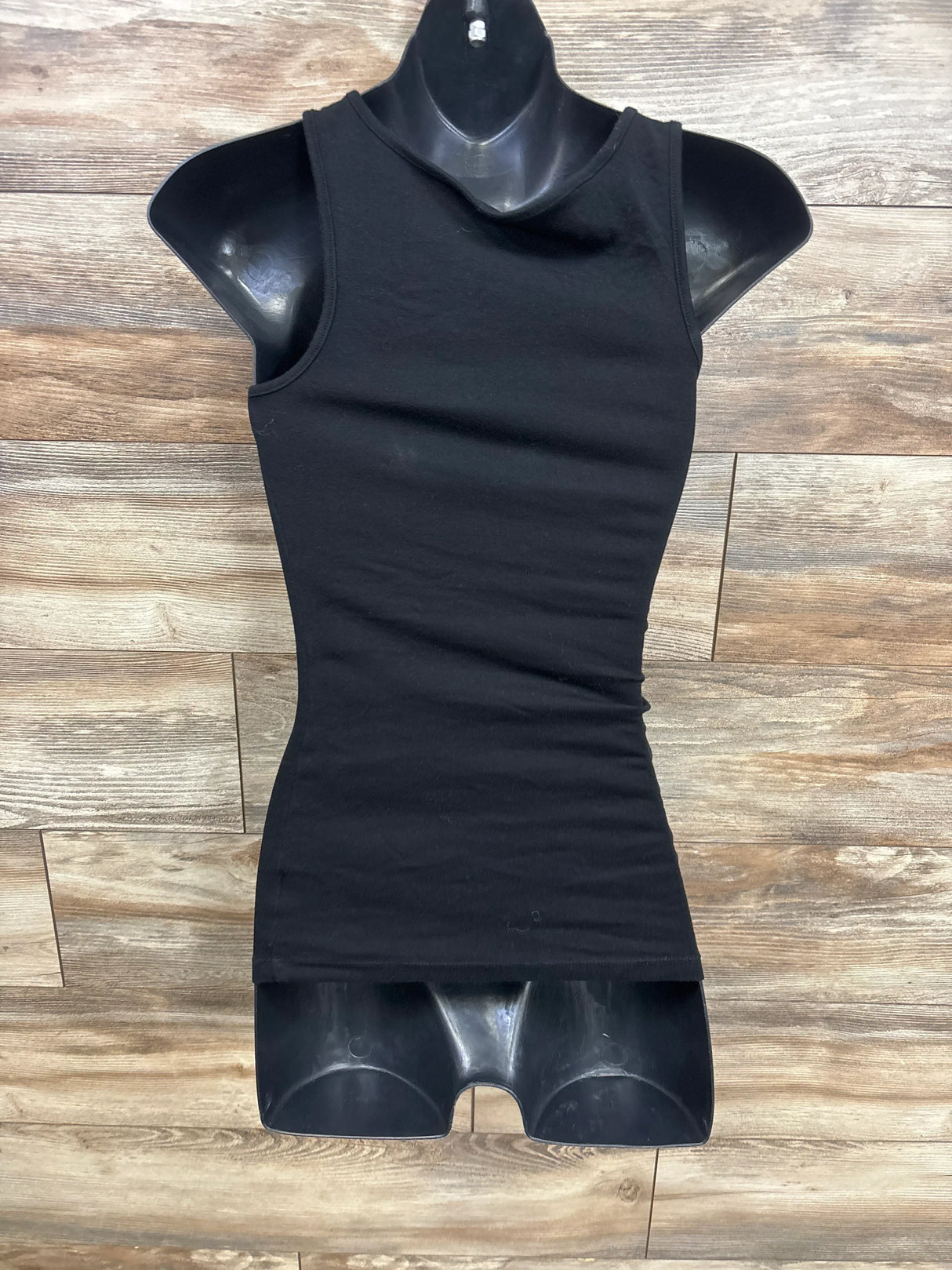 Black sleeveless tank top displayed on torso mannequin on wooden floor background