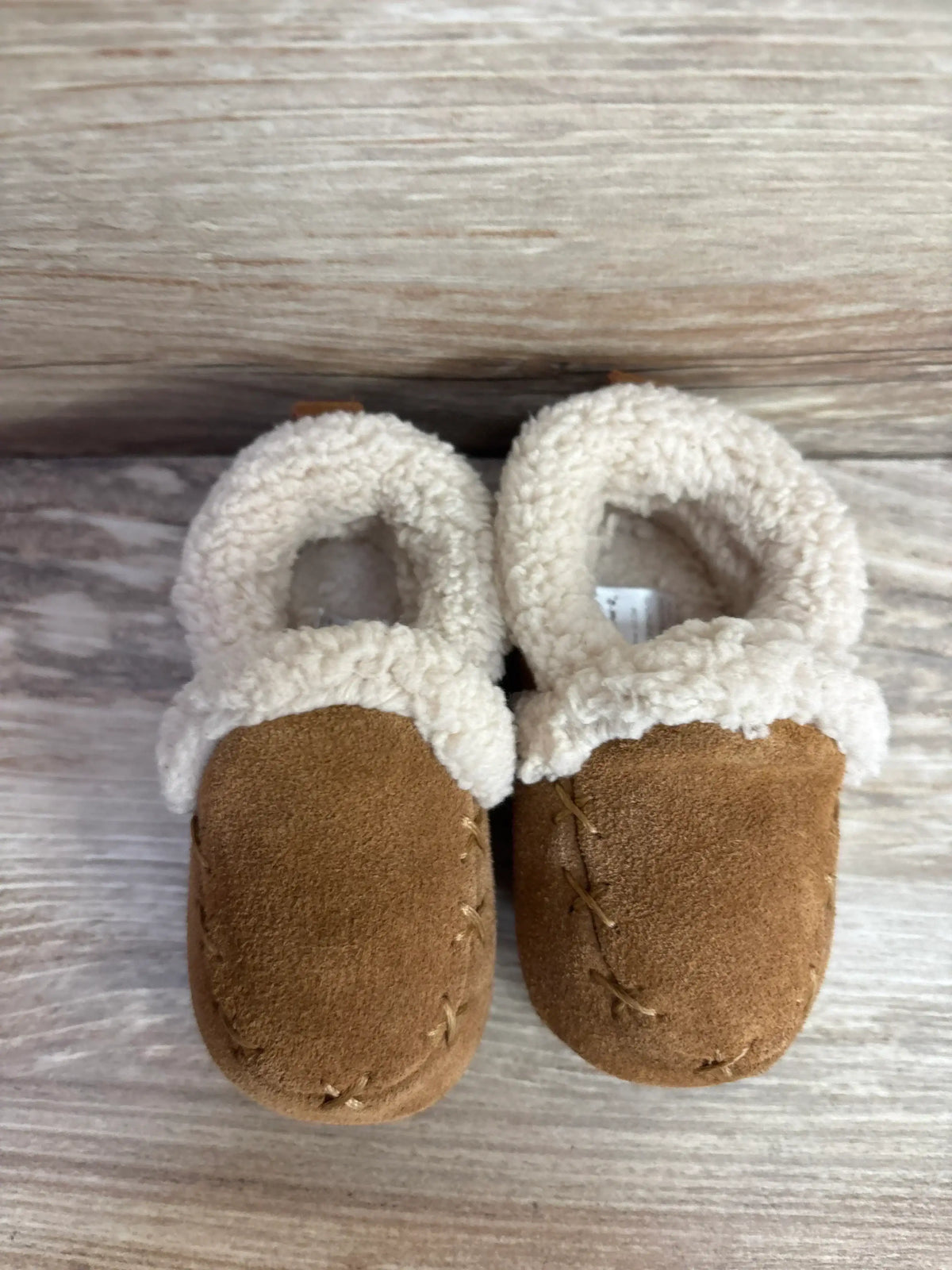 Pair of brown baby moccasin shoes with white fleece lining on wooden background