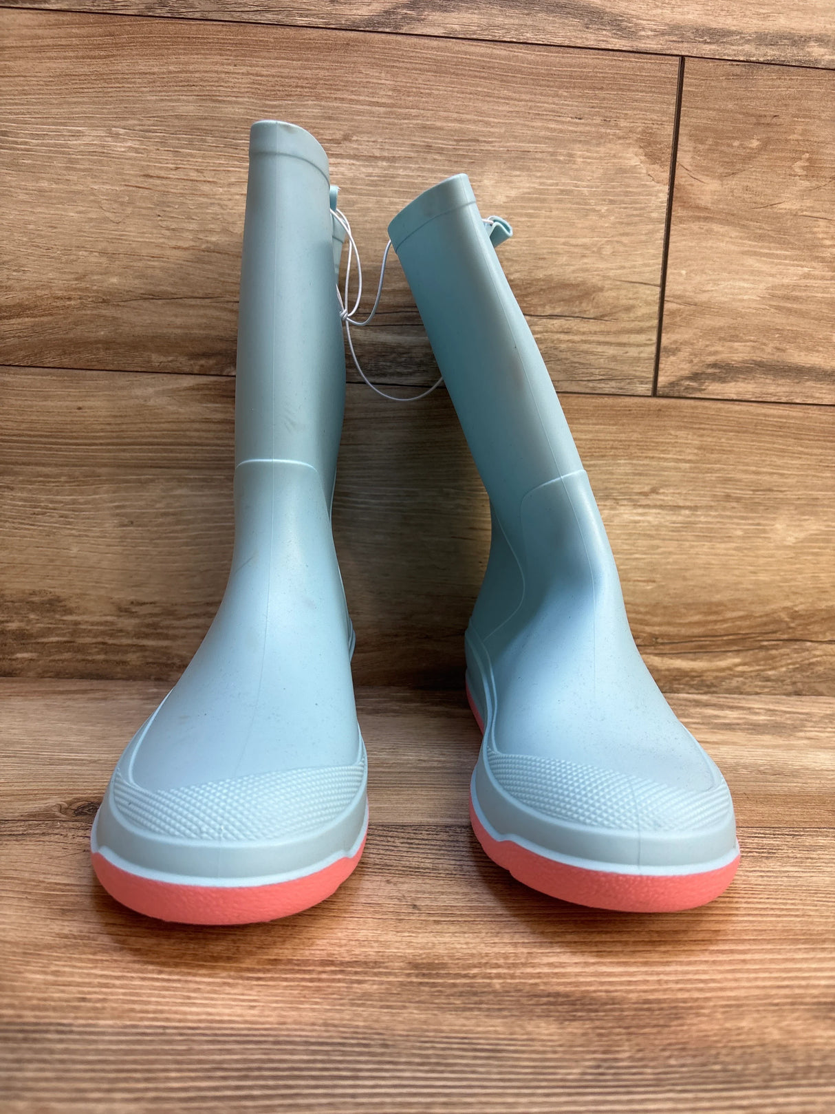 Light blue kids rain boots with pink soles on wood floor, front view