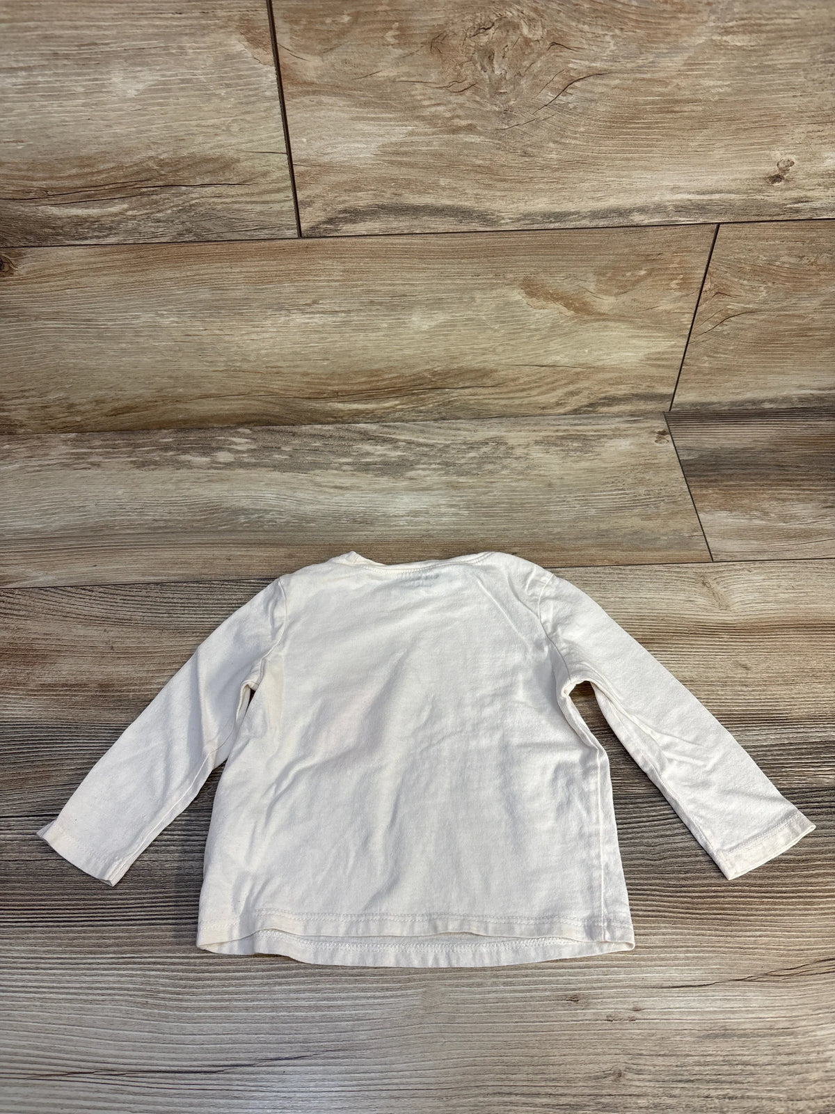 White long-sleeve kids shirt on wooden floor, ideal for baby and toddler clothing resale