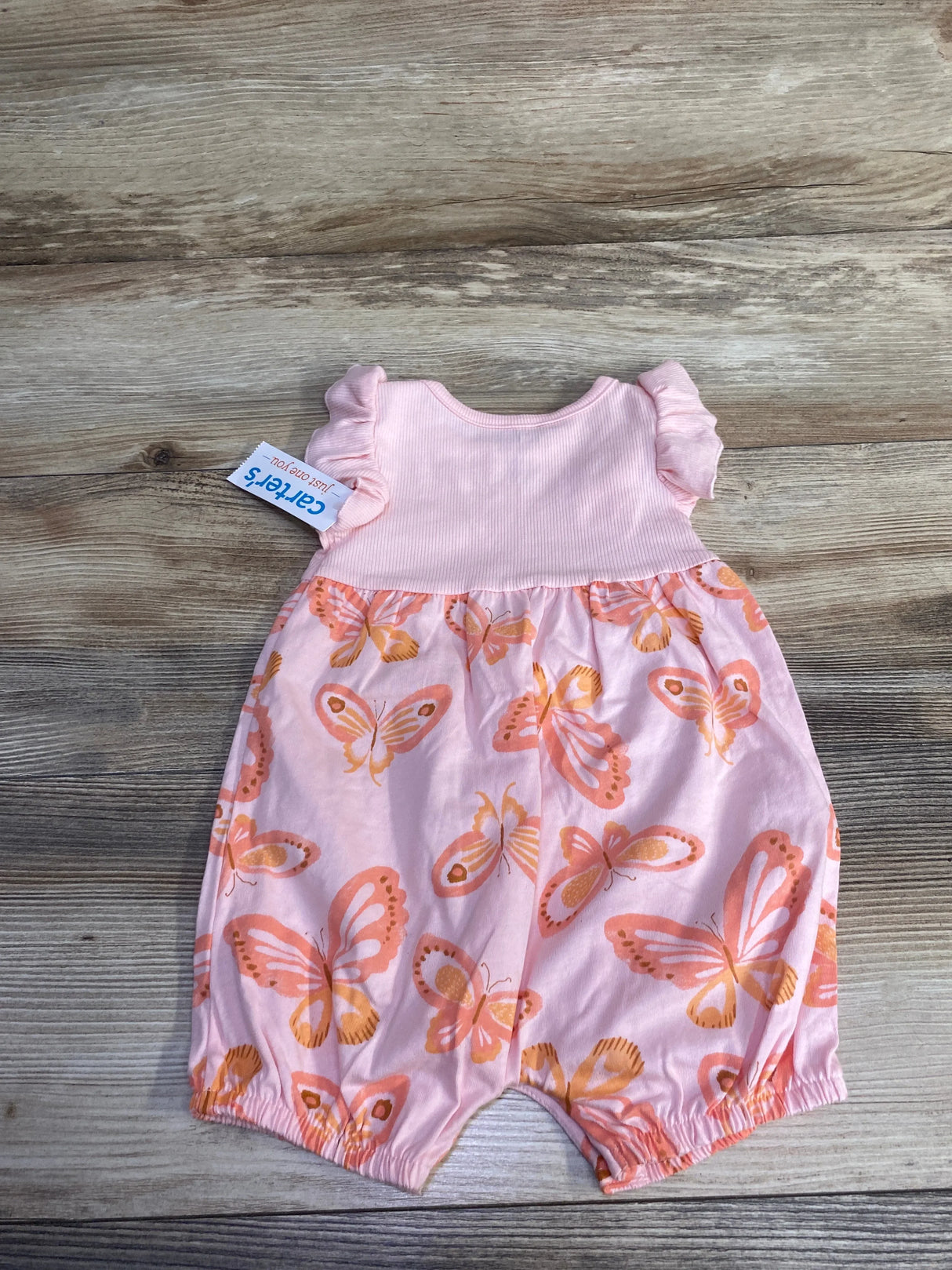 Front flat lay of Just One You sleeveless shortie romper with ribbed pink bodice, ruffle sleeves, and orange butterfly-print bottom on wood background